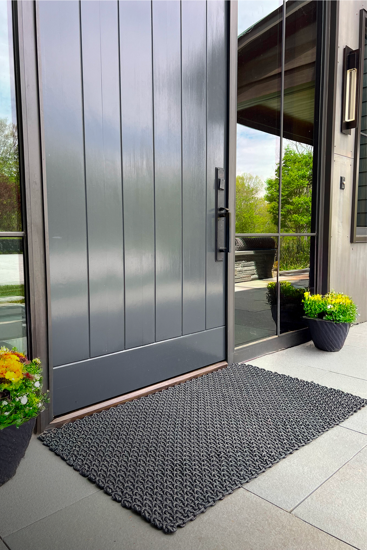 Modern front door with a doormat and potted plants on a sunny day.
